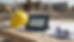 Close-up view of a rugged tablet showing a construction daily report beside a hard hat and marked drawings